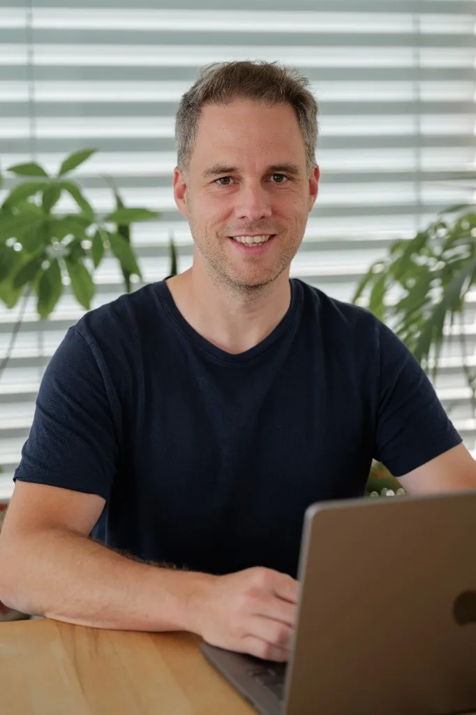Patrick Christen working on a laptop, smiling at the camera